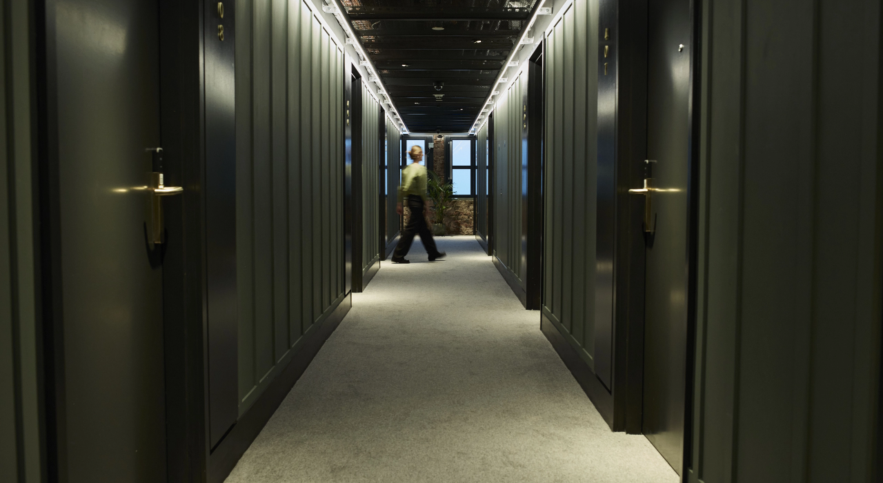 Dark green panelled apartment corridor with brass door handles, a person walking past an exposed brick wall